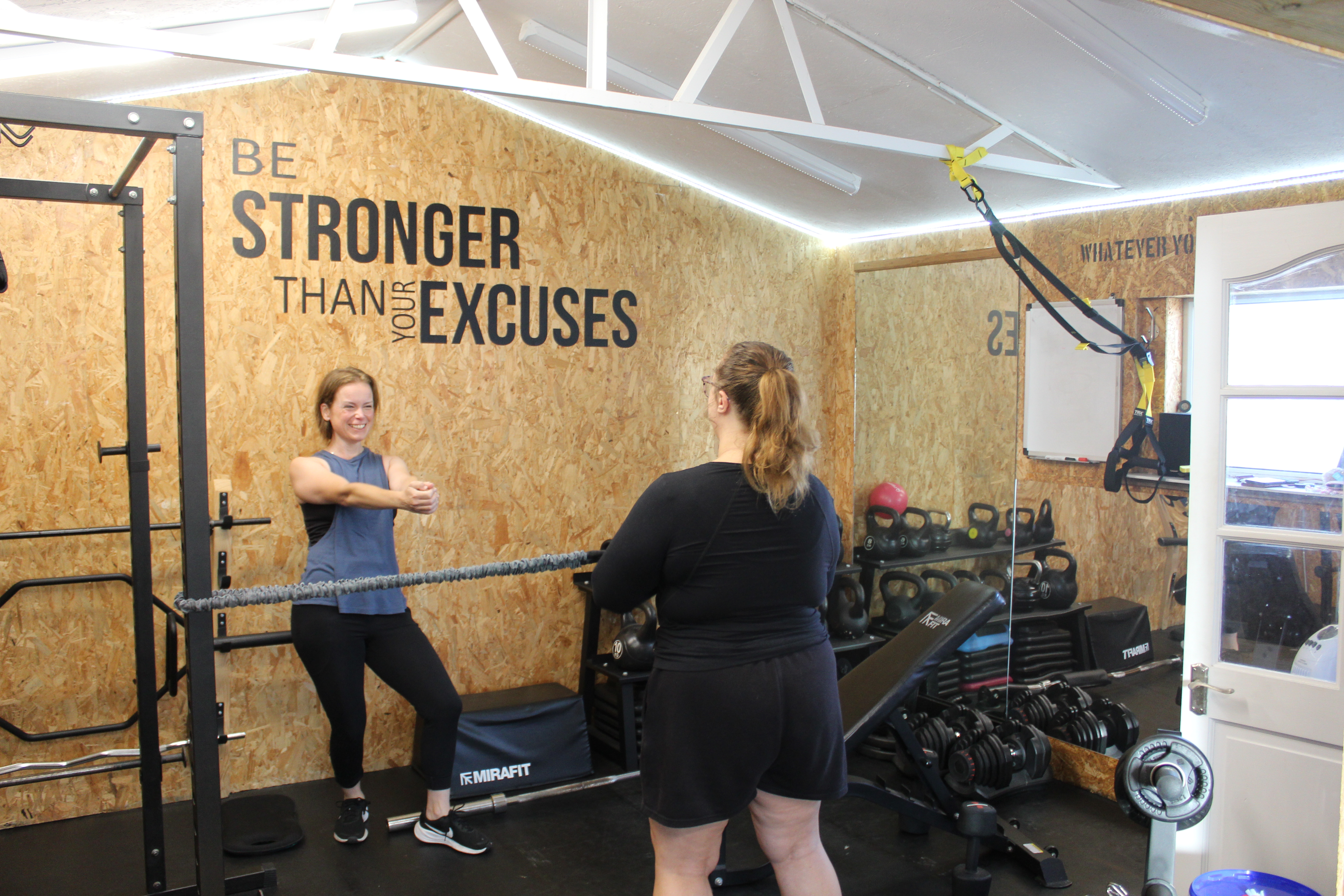 Esther guiding a client through a resistance band stretch beside the squat rack in the studio