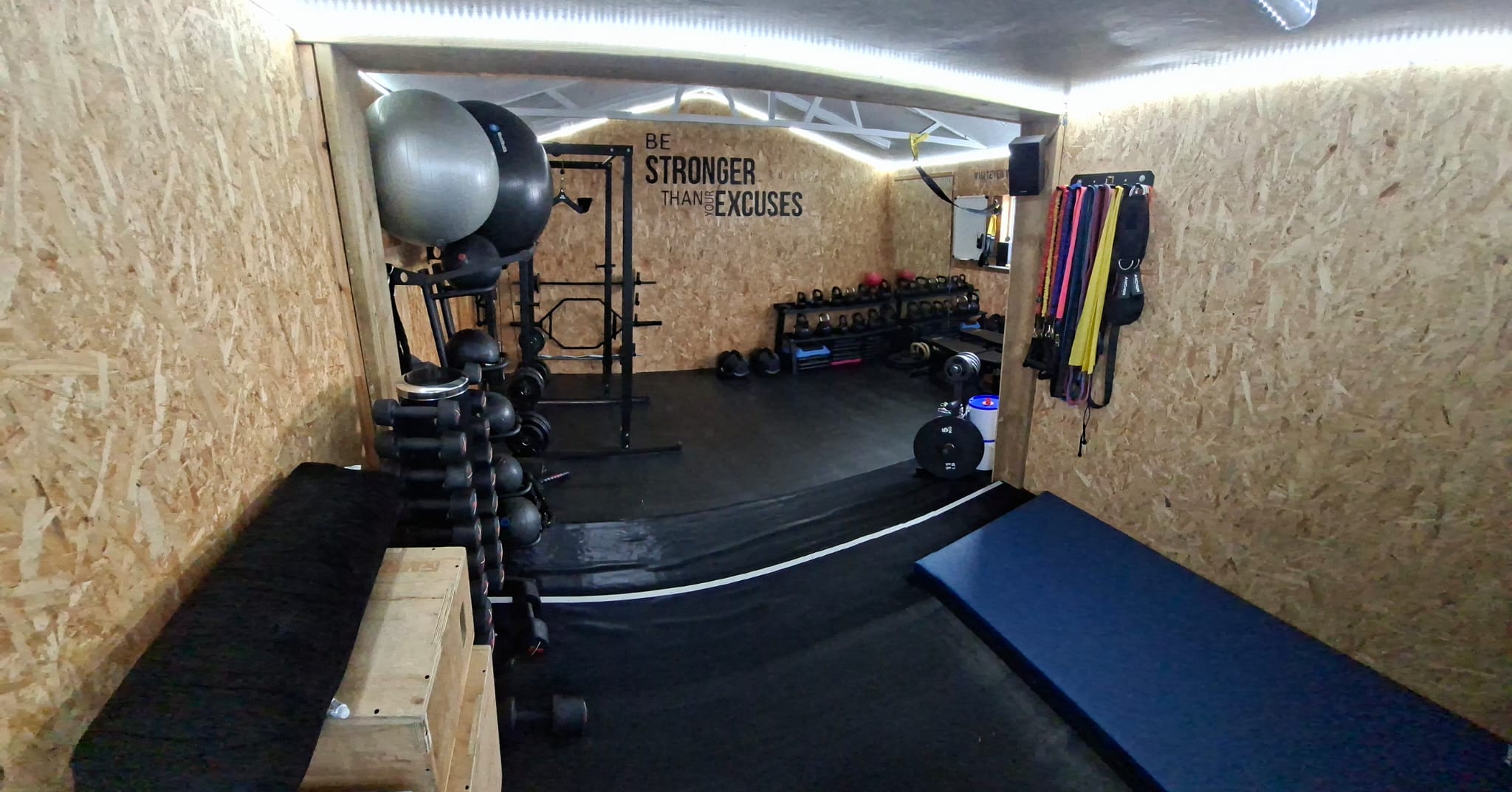 The private studio between sessions, empty: bare rubber matting on the floor with nothing left out on it, and weights, exercise balls and resistance bands stored on wall racks